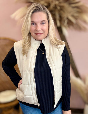 Woman wearing a cream quilted vest over a black top with a blurred indoor background