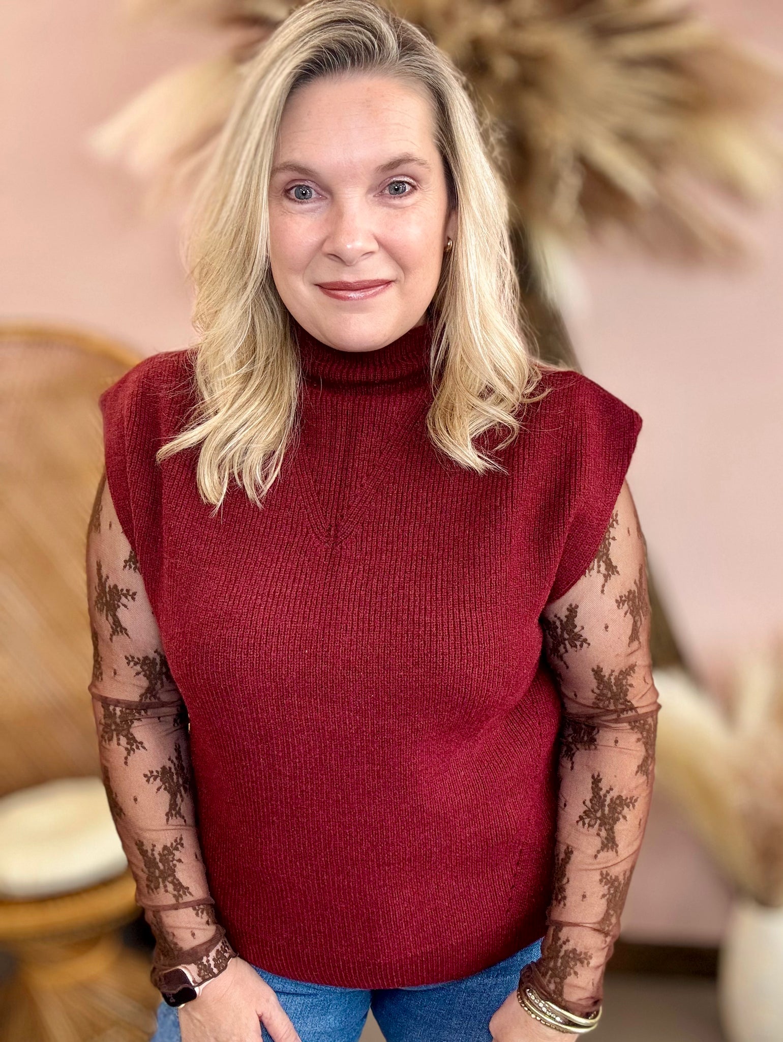 Woman wearing a red sleeveless sweater with floral arm coverings in a blurred indoor setting