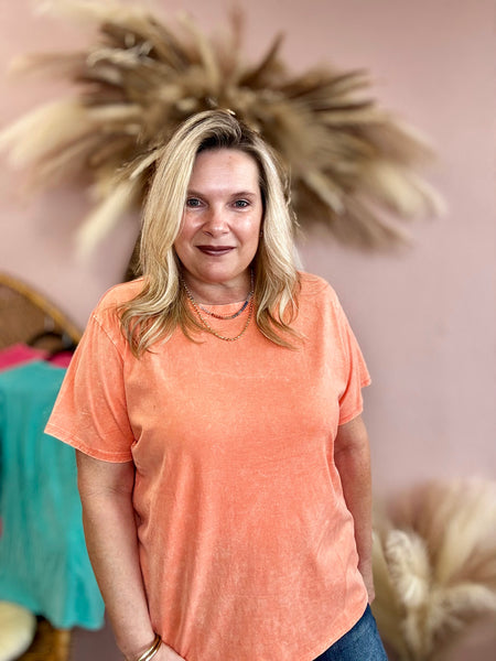 Woman wearing an orange t-shirt standing in a room with decorative elements.