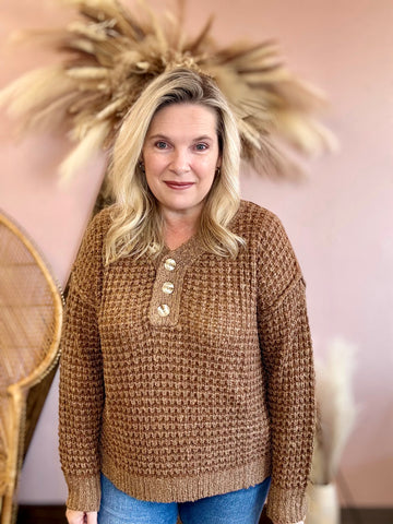 Woman wearing a brown knitted sweater with buttons in a decorative setting.