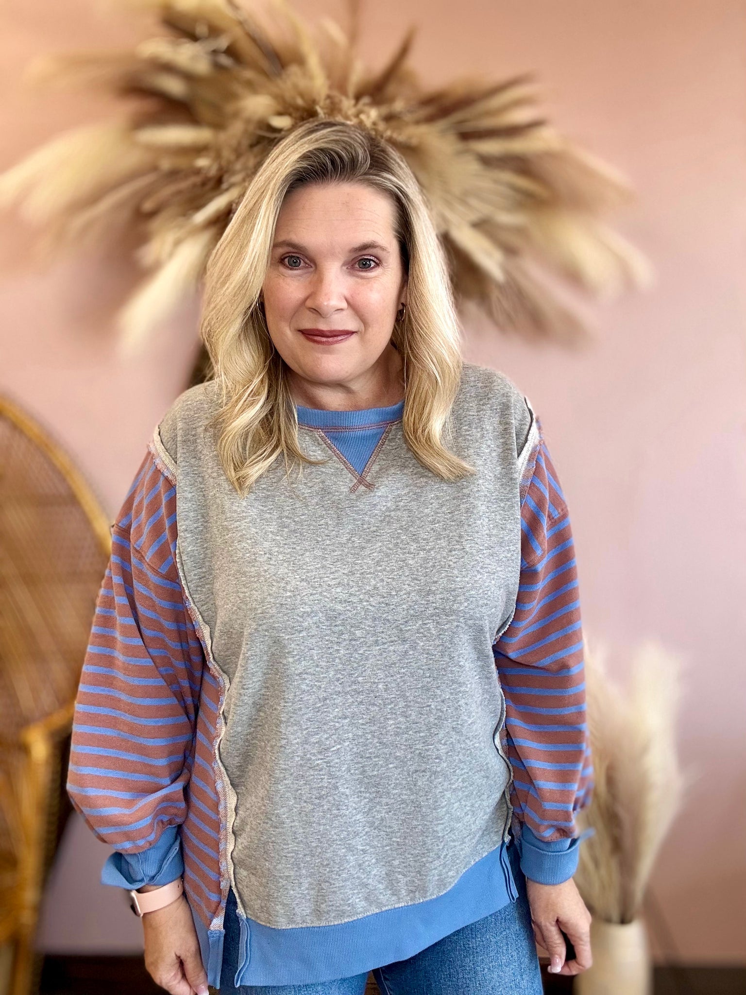 Woman wearing a gray sweater with striped sleeves against a decorative wall.