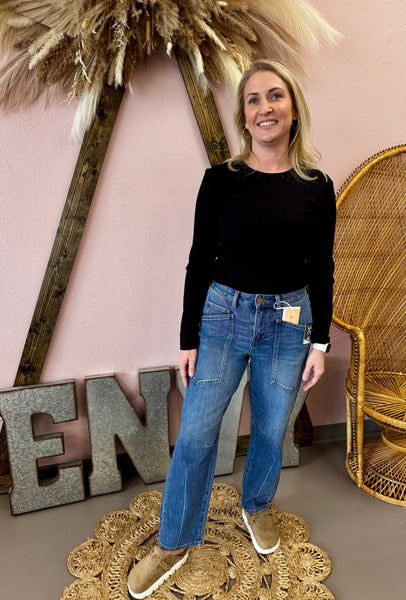 Woman in black top and blue jeans standing in front of decorative elements with a pink wall.