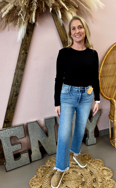 Woman in black top and blue jeans standing in a decorative room with 'ENY' letters.