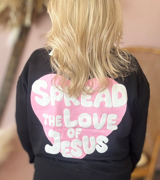 Person wearing a black shirt with a pink heart and white text on the back. Spread the love of Jesus.