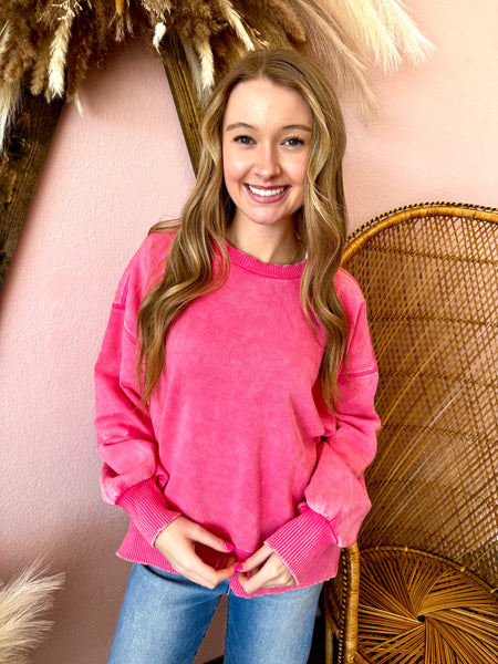 Woman wearing a pink sweater and blue jeans standing against a pink wall with decorative elements.