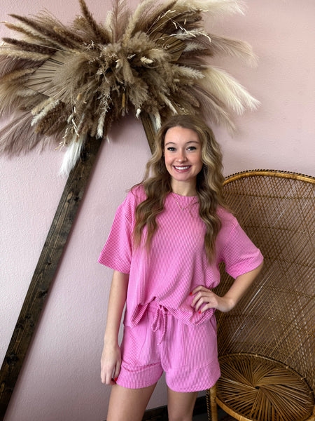 Woman in a pink outfit standing next to decorative elements on a pink wall