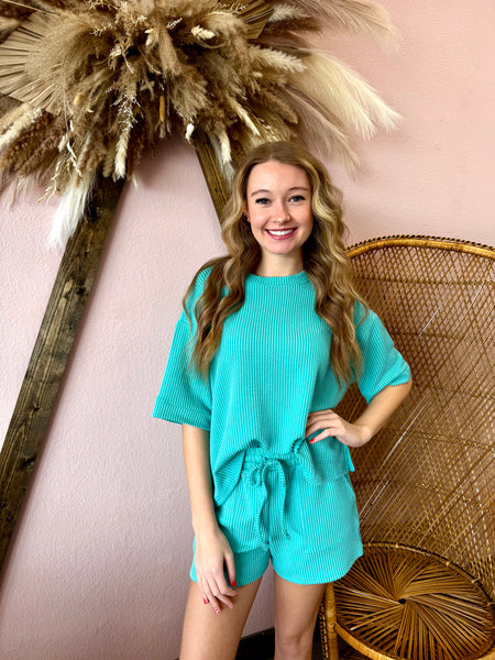 Woman in a teal outfit posing in front of decorative elements on a pink wall