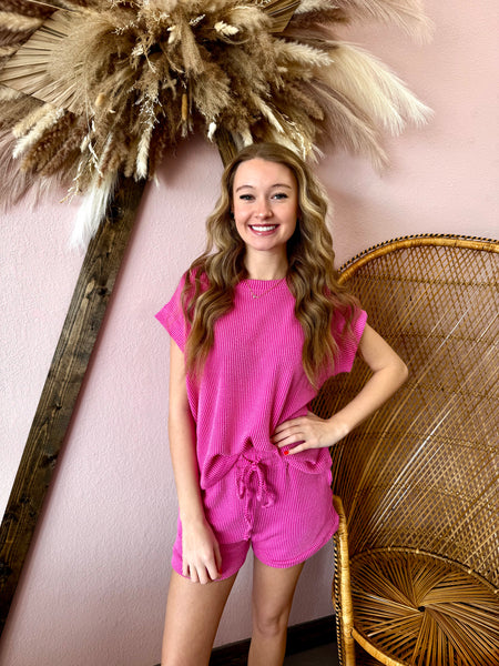 Woman in a pink outfit standing next to decorative elements on a pink wall