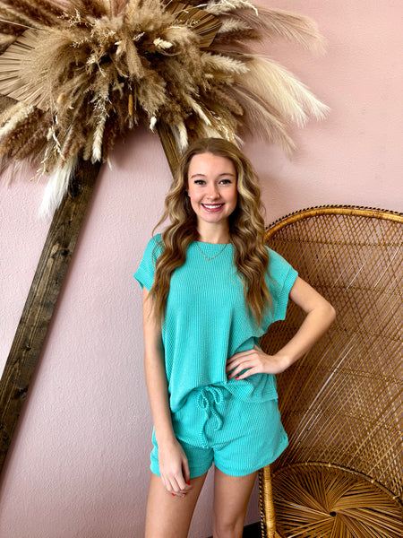 Woman in turquoise outfit posing in front of decorative elements on a pink wall