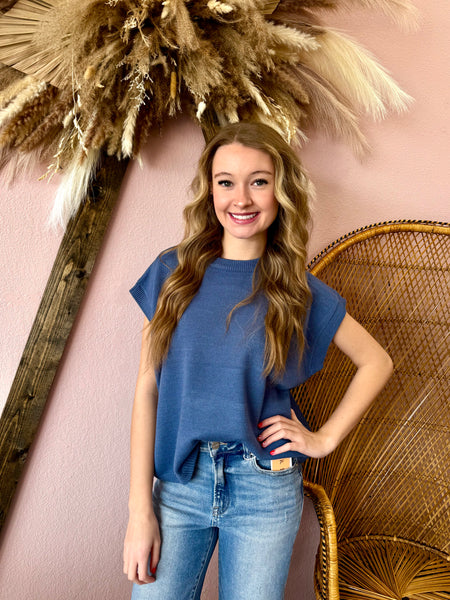 Woman in a blue top and jeans standing in front of decorative elements on a pink wall