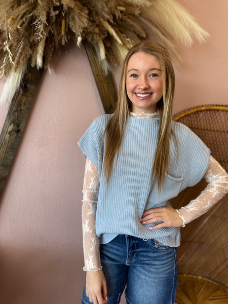 Woman wearing a light blue sweater with sheer sleeves against a pink wall.