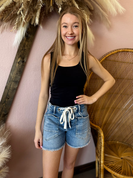 Woman in black tank top and denim shorts standing in front of decorative elements.