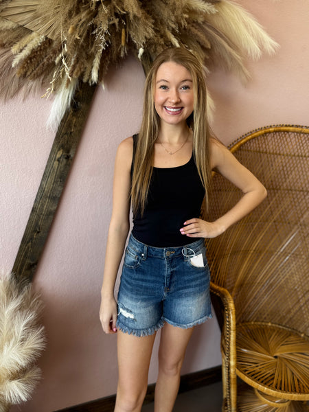 Woman in black tank top and denim shorts posing in front of decorative elements.