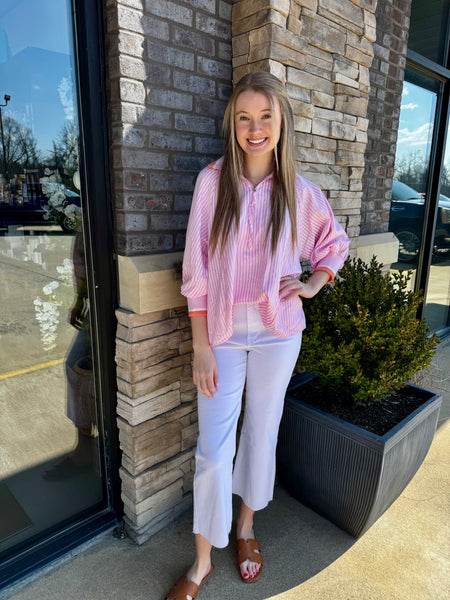 Woman in a pink shirt and white pants standing against a brick wall.