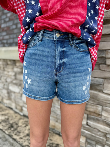 Person wearing blue denim shorts with white star patterns and a red sweater with a blue plaid pattern.