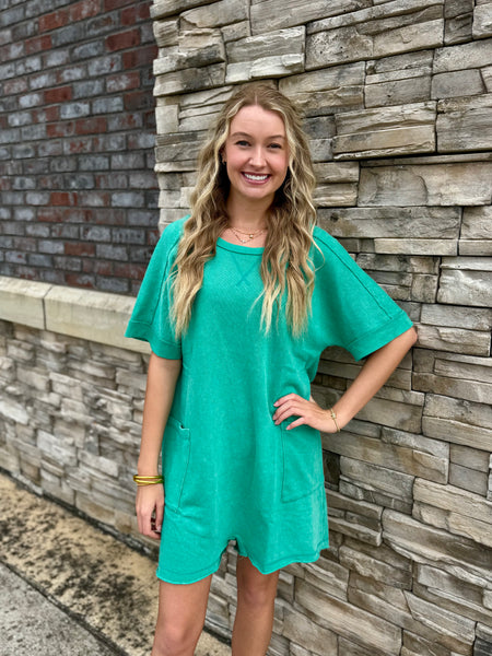 Woman in a teal dress standing against a stone wall