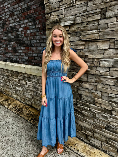 Woman in a blue dress standing against a stone wall.
