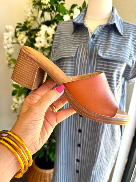 Person holding a brown sandal with wooden heel in front of a mannequin wearing a blue and white striped shirt.