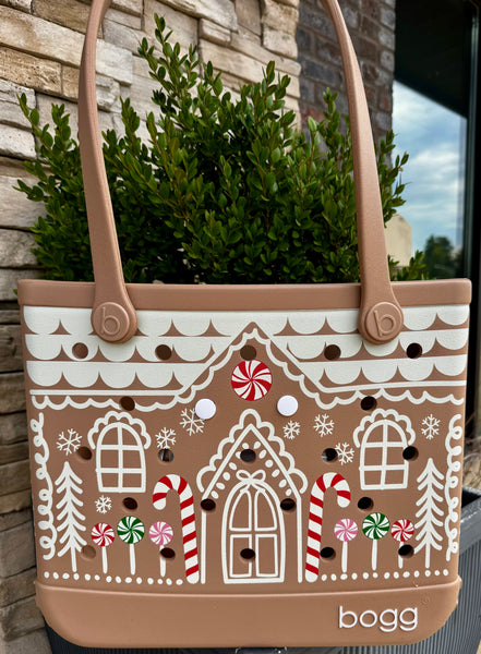 Tote bag with gingerbread house design and 'bogg' branding against a stone wall background