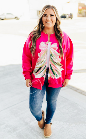 Woman wearing a bright pink cut sweatshirt cardigan with a colorful tree design, standing on a sidewalk.